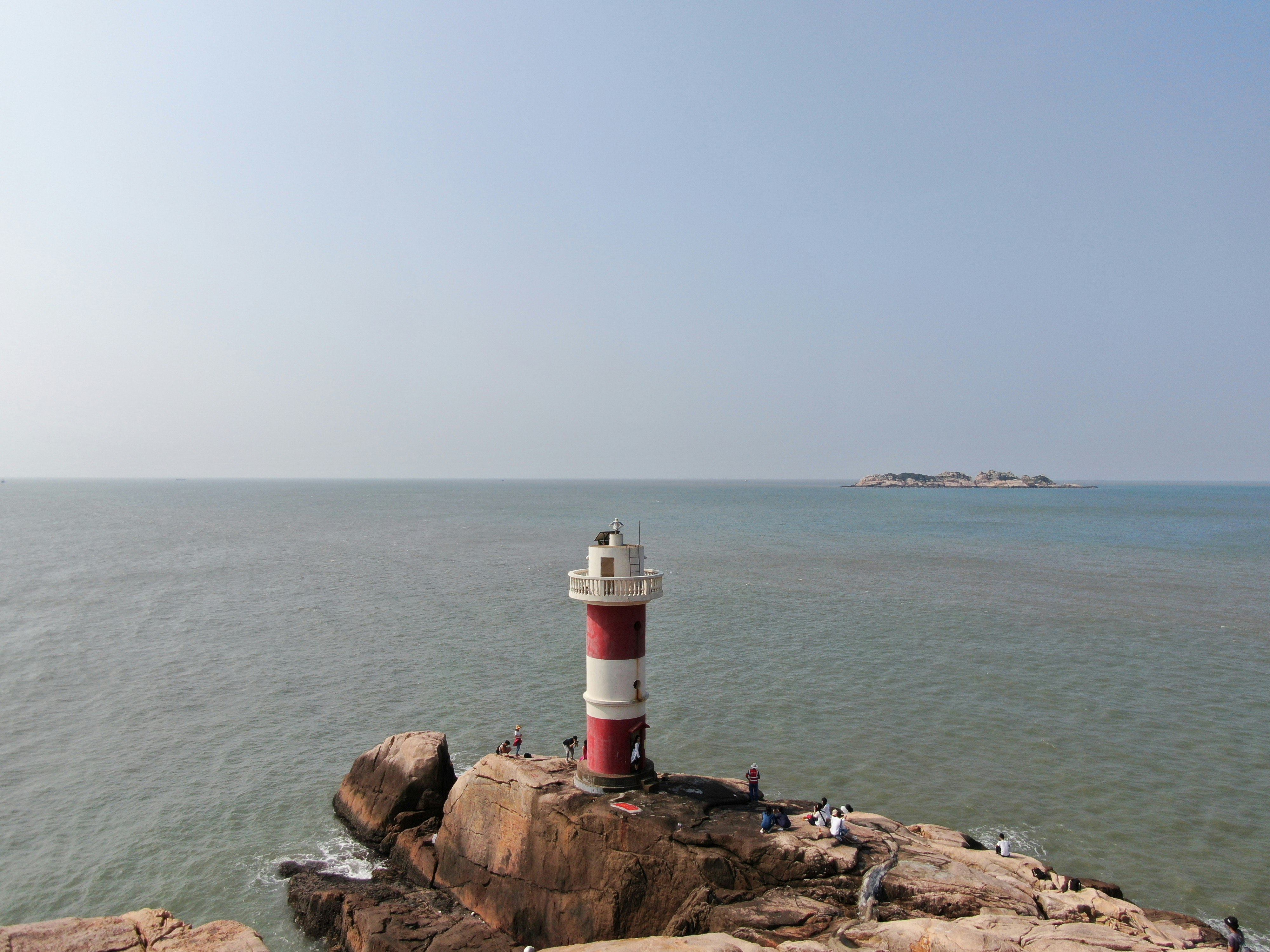 white and red lighthouse on brown rock formation near body of water during daytime